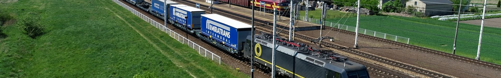 Pociąg z naczepami Miratrans Intermodal jadący po torach. W tle widać Multimodal Terminal Miratrans.